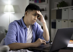 Unhappy young Asian man looking at laptop screen with serious and worried